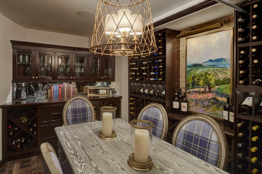 A custom wine cellar with gold trimmed blue chairs, a table with gold trimmed candles, and overhead lighting.