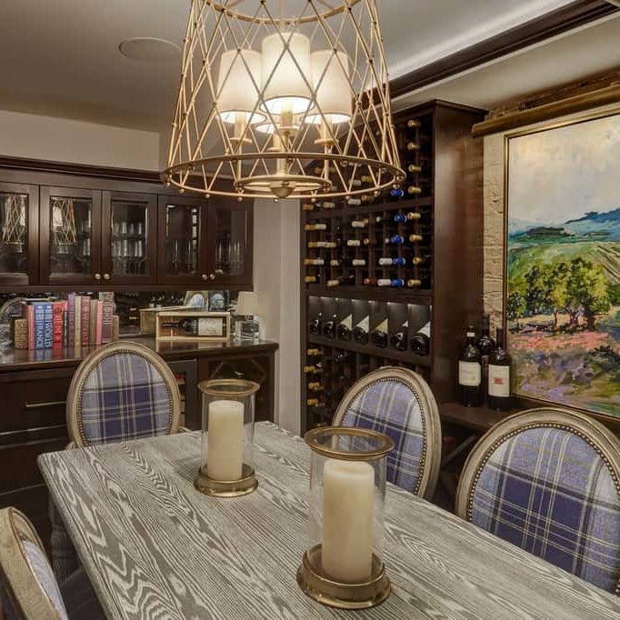 A custom wine cellar with gold trimmed blue chairs, a table with gold trimmed candles, and overhead lighting.
