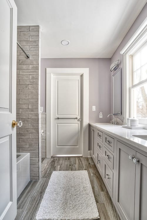 A gray and white Jack and Jill Bathroom with wooden floors and a stone tiled bath