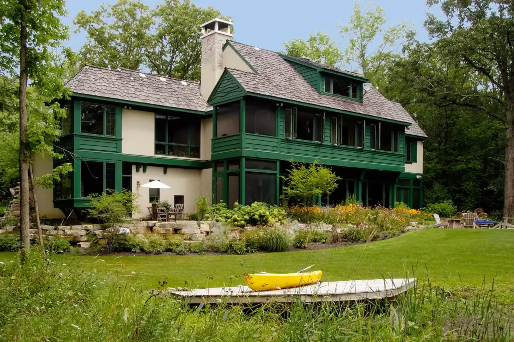 Picture of a backyard view of a green house with a yellow boat near the water