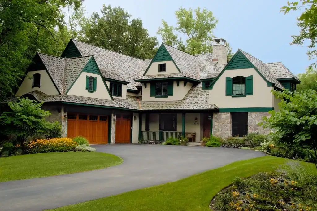 Picture of a large custom home renovation with green trim and a paved circular driveway