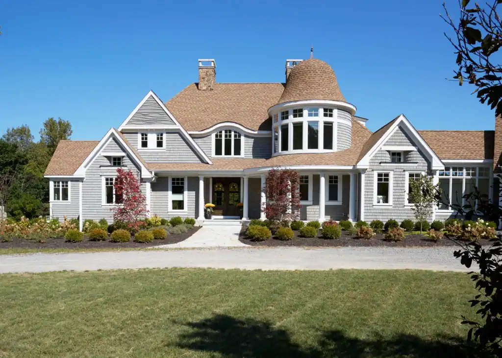 Picture of a large grey shingled house featuring white trim and a prominent rounded turret