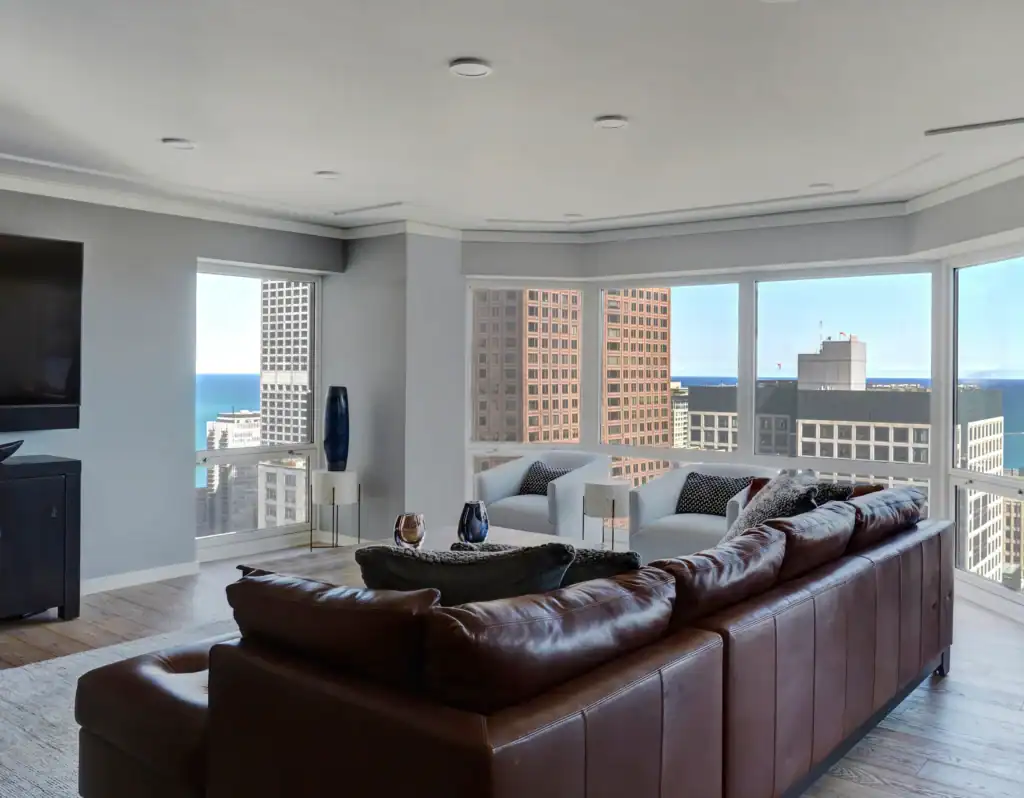 Picture of a spacious living room with a brown leather sectional and city skyline views.