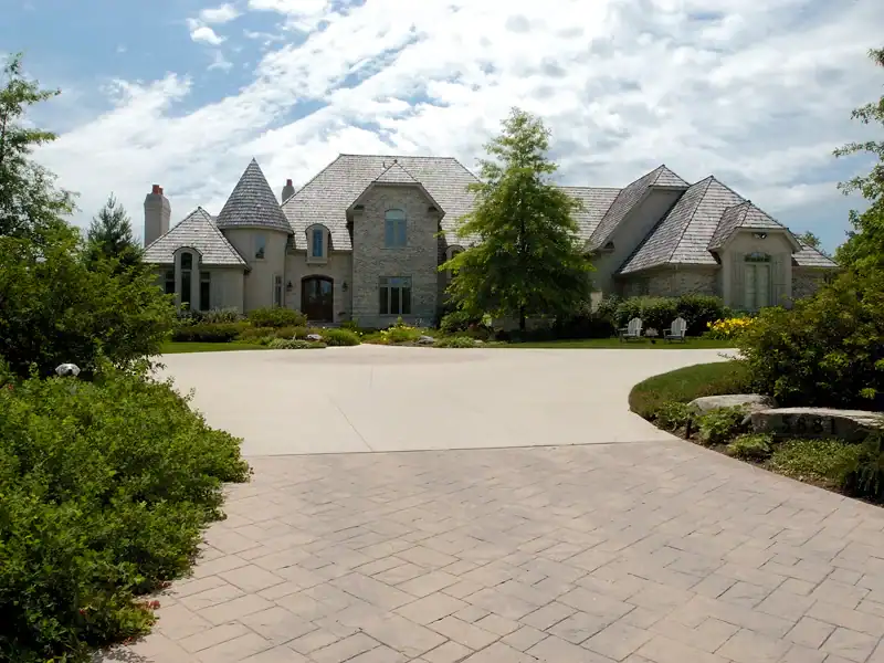 Picture of a sprawling grey stone house with a circular paved driveway and mature landscaping