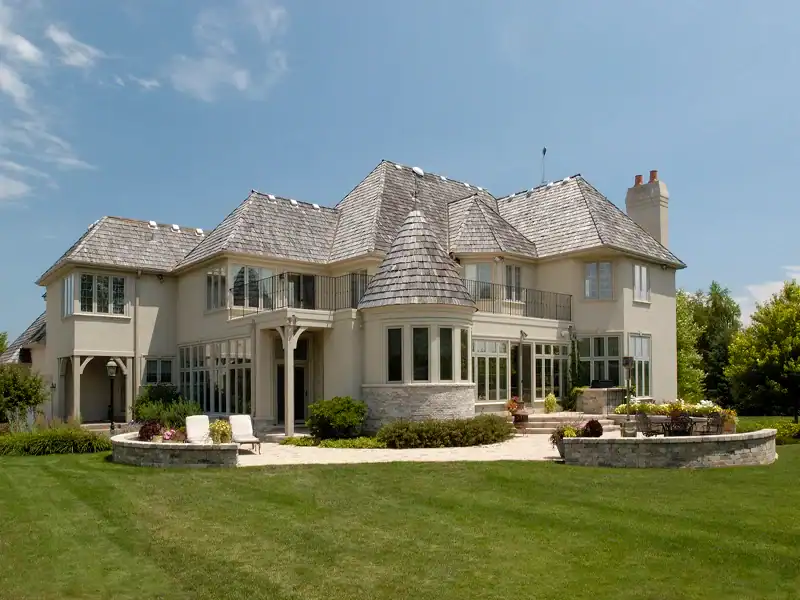 Picture of the backyard of a large tan house after a custom home renovation with a curved stone patio