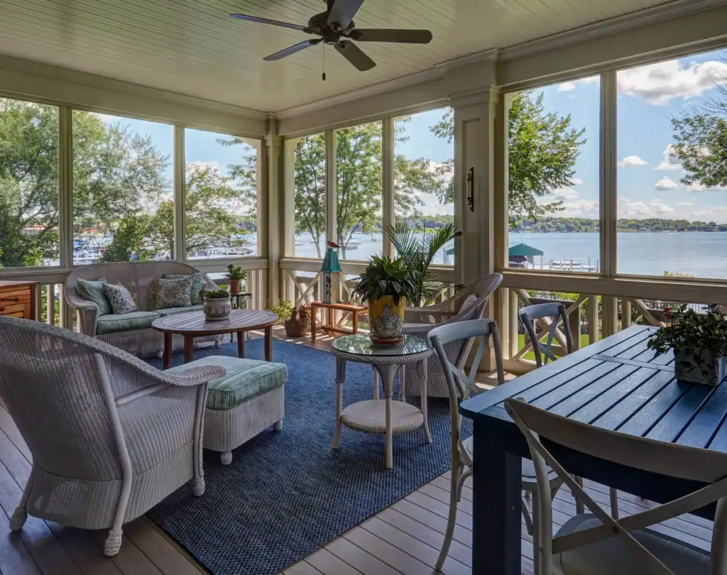 Picture of a screened porch furnished with wicker seating overlooking the water.