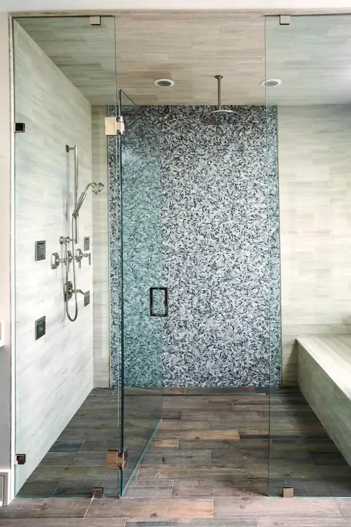 Picture of a walk-in glass shower featuring a pebble mosaic accent wall and wood-look floor tiles