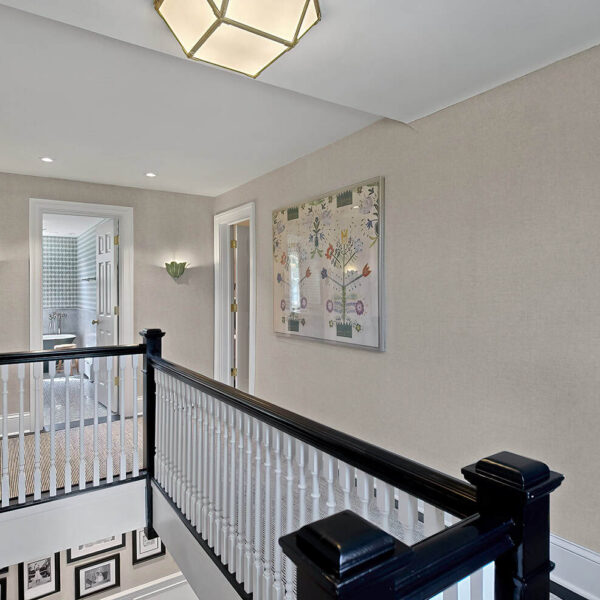 Second floor landing featuring grasscloth wallpaper, custom millwork, decorative sconces, and black-and-white stair railing.